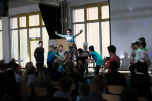 Schüler führen auf einer Bühne eine Theateraufführung vor Publikum auf.