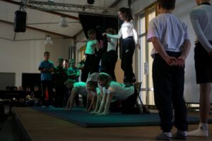 Gruppe von Schülern führt eine Gymnastik-Übung auf einer Bühne vor Publikum vor.