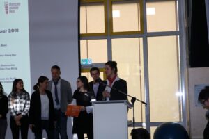 Schüler präsentiert auf einer Bühne vor einer Gruppe von Mitstudenten.