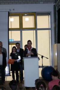 Eine Person spricht am Rednerpult vor einer Gruppe von Zuhörern.