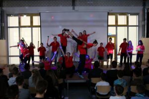Schüler führen eine Theateraufführung vor, mit bunten Lichtern und einem Publikum.