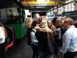 Menschenmenge in einer Halle, Ausstellerstände und ein grüner Bus im Hintergrund.