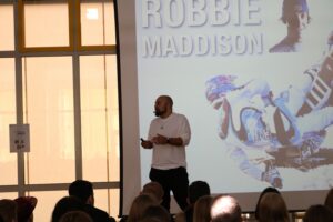 Ein Mann steht vor einer Präsentation über Robbie Maddison.