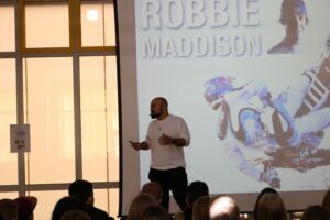 Ein Mann steht vor einer Präsentation über Robbie Maddison.
