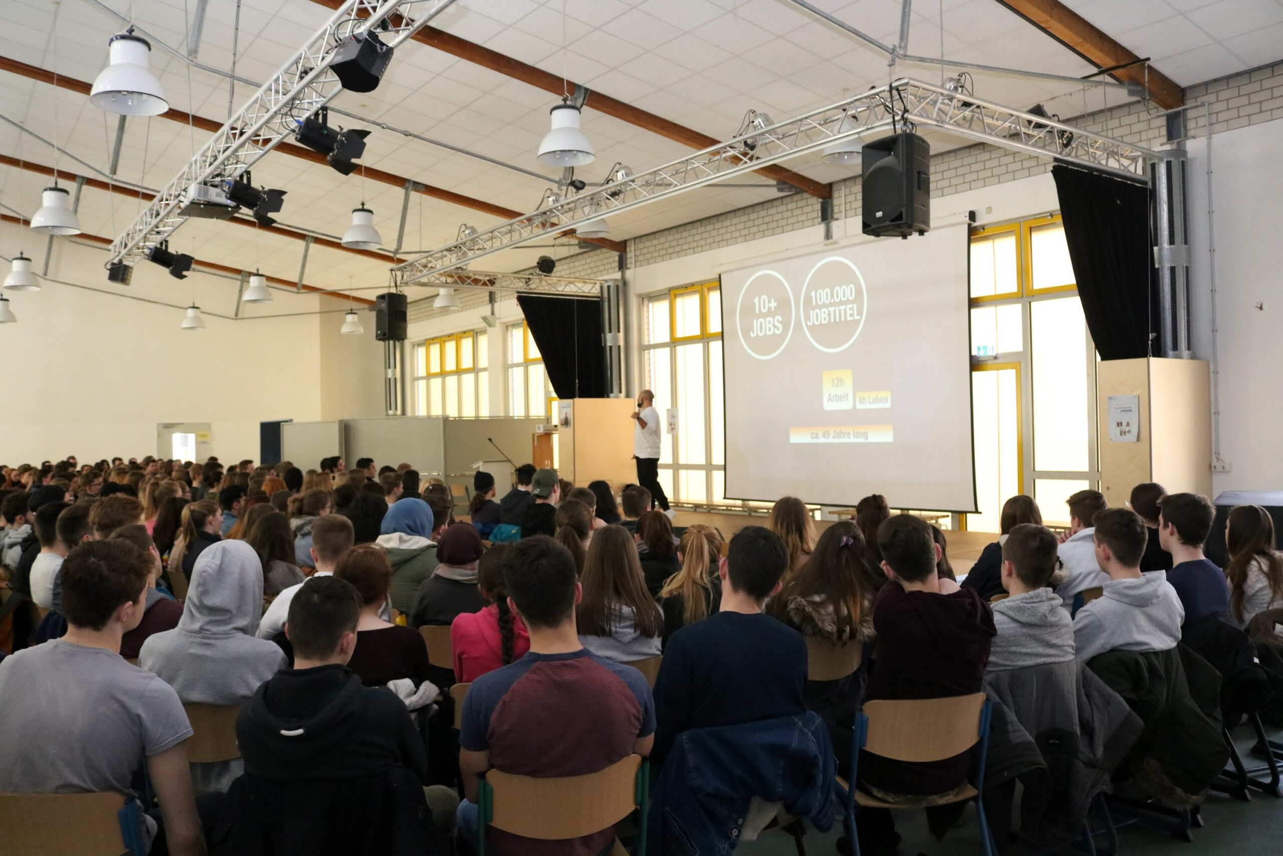 Schüler sitzen in einem großen Raum und hören einem Vortrag zu.