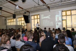 Vortragender steht vor einer großen Gruppe von Schülern in einem Klassenraum.