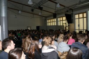 Schüler hören aufmerksam einem Vortrag in einem großen Raum zu.
