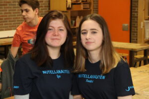 Zwei Mädchen mit T-Shirts sitzen an einem Tisch in einem Klassenzimmer.