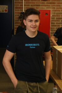 Schüler in T-Shirt steht lächelnd vor einer Wand mit Werkzeugen.