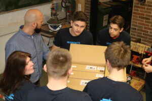 SchülerInnen diskutieren an einem Tisch, umgeben von Kartons und Geräten.