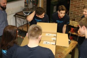 Schüler besprechen Aufträge an einem Tisch mit Kartons und Werkzeug.