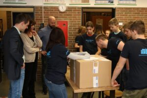 Schüler und Erwachsene versammeln sich um einen Tisch mit einem großen Karton.