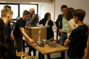 Gruppe von Schülern und Lehrern bespricht Robotermodelle an einem Tisch.