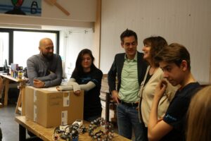 Gruppengespräch in einem kreativen Klassenraum mit Robotern und einem Karton.