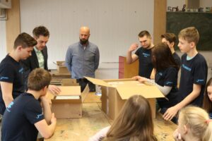 Schüler sitzen an einem Tisch und betrachten Inhalte aus zwei Kartons.