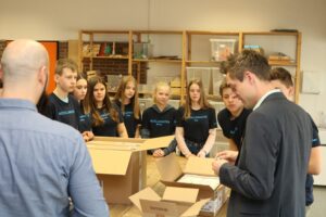Schülerinnen und Schüler stehen um einen Tisch mit Kartons in einem Klassenraum.
