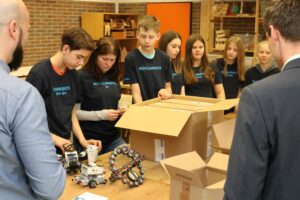 Schüler arbeiten an Robotern und öffnen einen Karton in einem Unterrichtsraum.