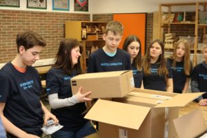 Schüler*innen packen Kartons in einer Werkstatt. Teambekleidung sichtbar.
