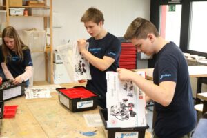 Schüler bauen Modelle in einem Werkraum und nutzen Materialien aus Kisten.