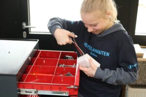 Ein Mädchen mit Schraubenzieher öffnet eine Box in einem Werkstattwagen.