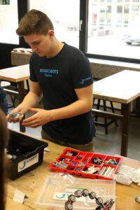 Ein Schüler arbeitet an einem Tisch mit Robotik-Bauteilen und Werkzeugen.