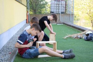 Drei Schüler arbeiten draußen an einem Holzprojekt.