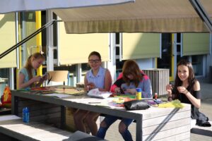Vier Schülerinnen sitzen an einem Tisch und basteln in der Sonne.