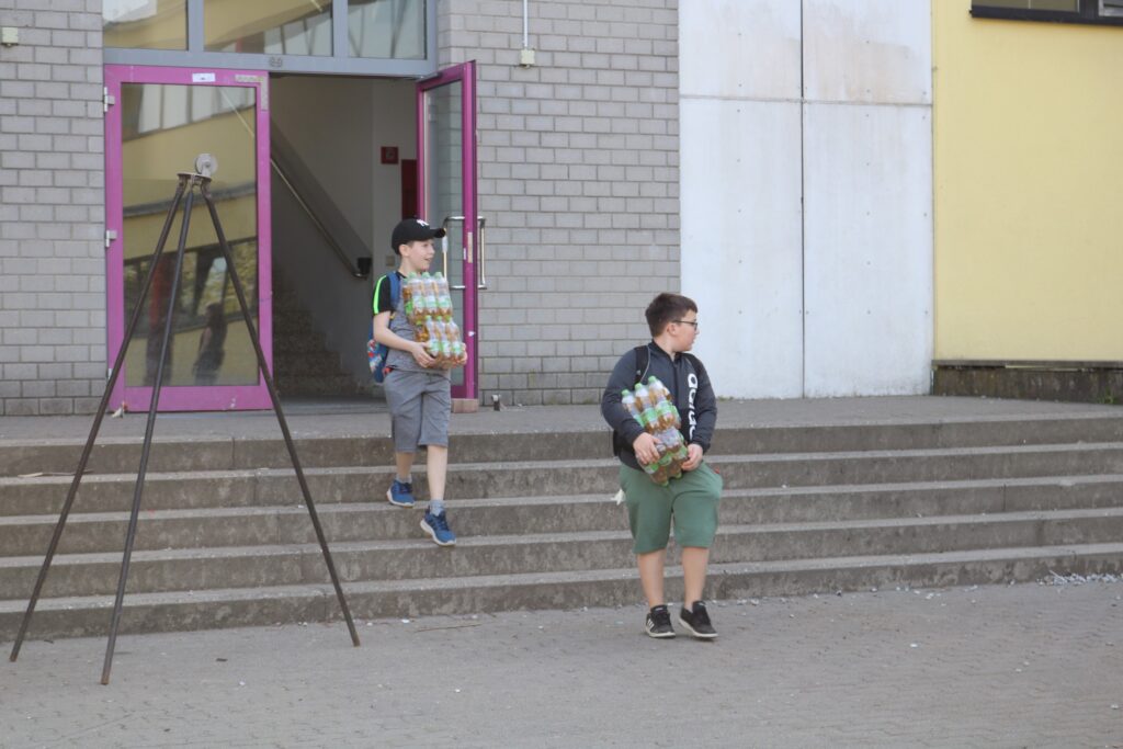 Zwei Kinder tragen Getränke und kommen die Treppe einer Schule herunter.