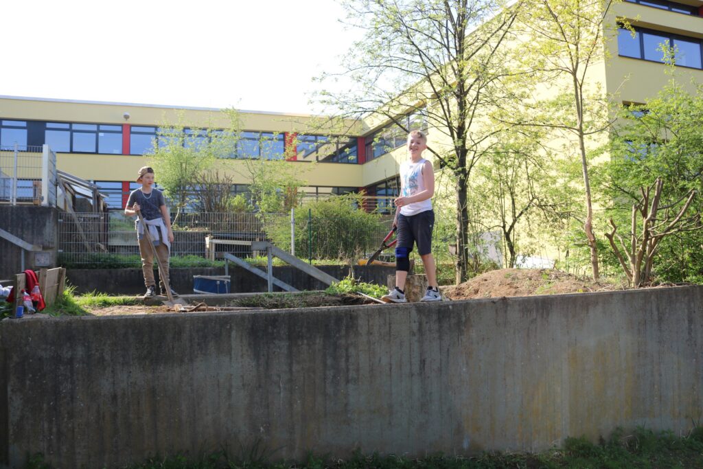 Schüler arbeiten im Freien an einem Gartenprojekt vor einem Schulgebäude.