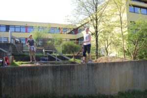 Schüler arbeiten im Freien an einem Gartenprojekt vor einem Schulgebäude.