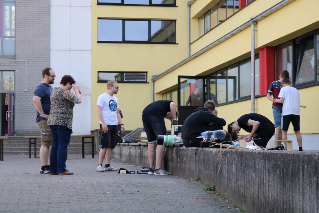 Gruppe von Personen arbeitet an einem Projekt im Freien vor einem Gebäude.