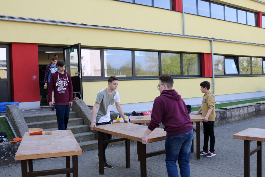 Schüler tragen Tische aus einem Schulgebäude nach draußen.