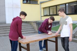 Drei Schüler stehen um einen Tisch und arbeiten gemeinsam daran.
