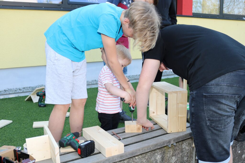 Kinder bauen mit Holzklötzen und Werkzeug im Freien.