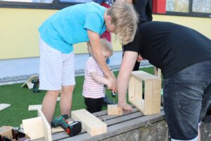 Kinder bauen mit Holzklötzen und Werkzeug im Freien.