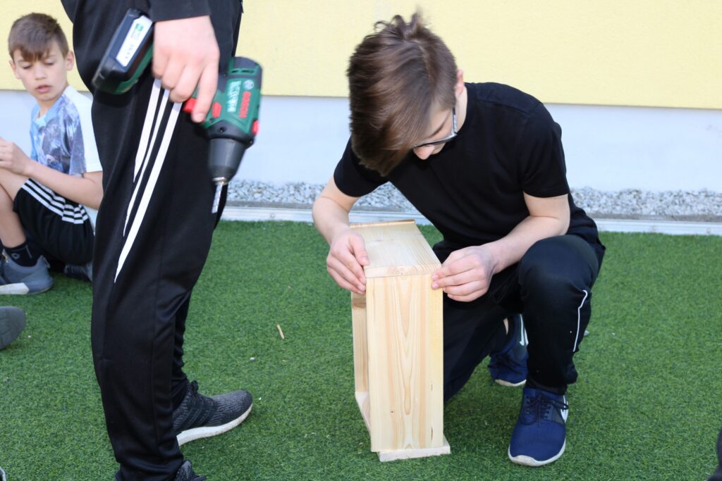 Schüler arbeitet an einem Holzprojekt, während andere zuschauen.