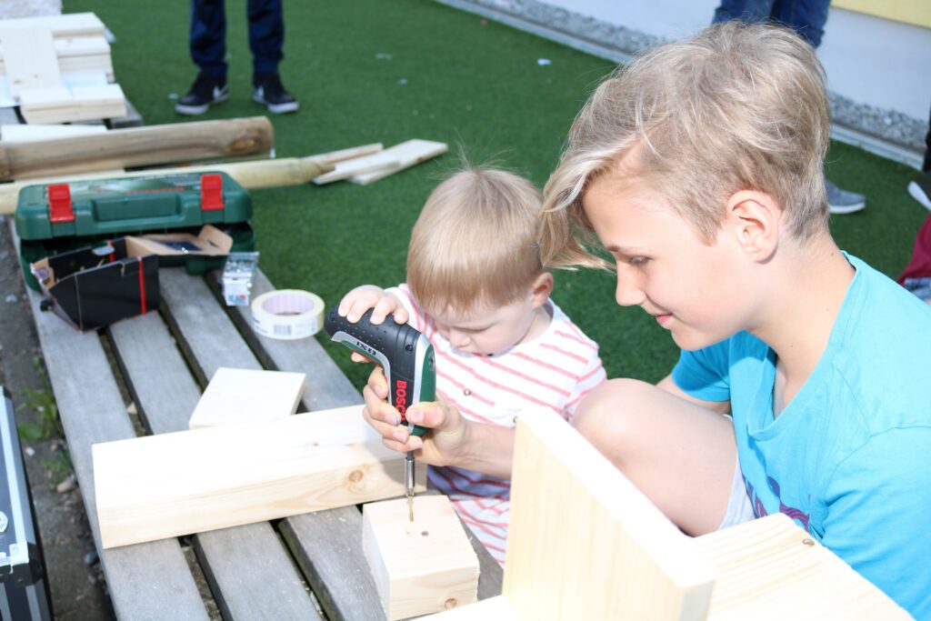 Kinder arbeiten gemeinsam mit Werkzeugen an einem Holzprojekt im Freien.