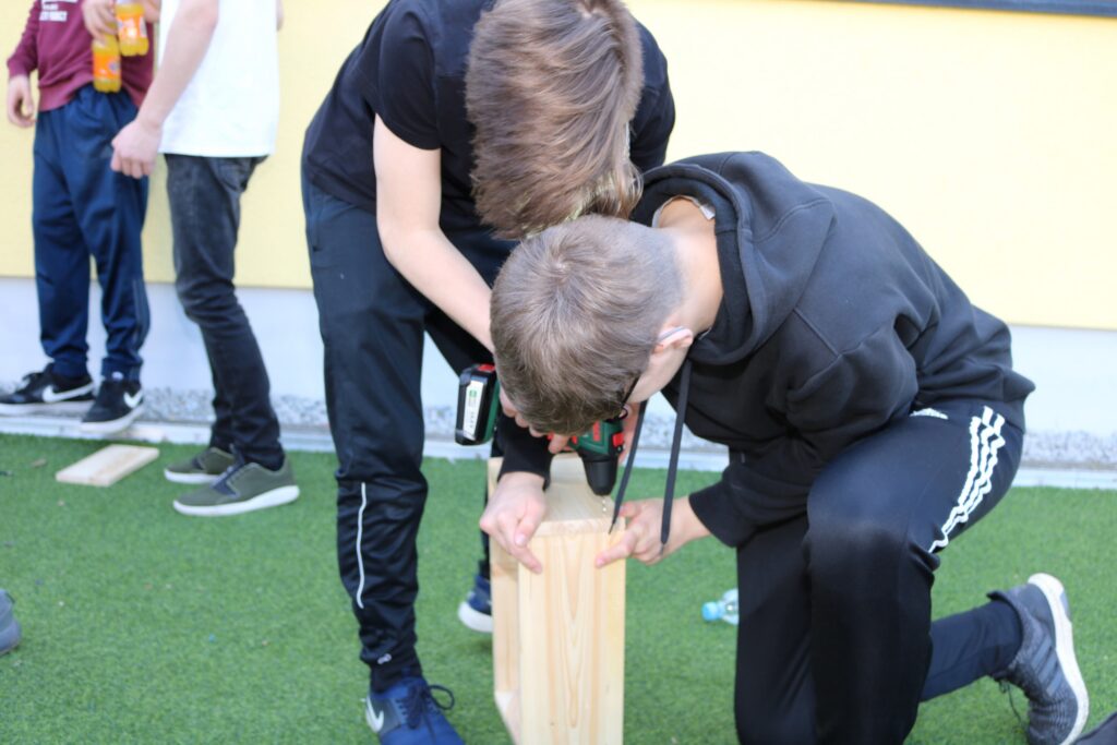 Zwei Schüler arbeiten zusammen an einem Holzprojekt im Freien.
