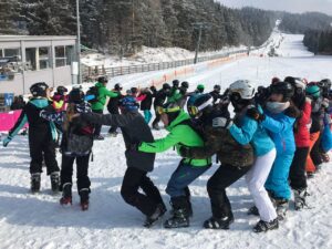 Schülerinnen und Schüler stehen in einer Reihe im Schnee und üben Skifahren.