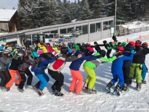 Schüler in bunter Skibekleidung bilden eine Kette im Schnee.