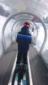 Kind auf Ski in einem Förderband-Tunnel im Schnee.