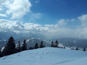 Winterliche Berglandschaft mit schneebedeckten Hügeln und wolkenverhangenem Himmel.