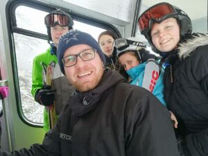 Gruppe von Skifahrern im Lift, lächelnd und mit Helmen und Brillen.