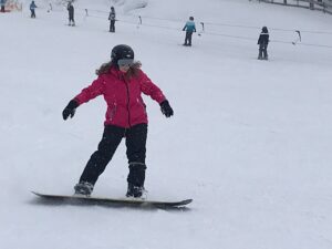 Ein Mädchen in pinker Jacke snowboardet auf einer verschneiten Piste.