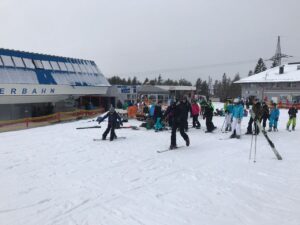 Skigebiet mit Wartenden an der Talstation, Schnee und mehrere Skifahrer.
