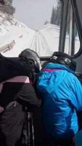 Zwei Kinder sitzen nebeneinander in einem Fahrzeug und schauen aus dem Fenster auf verschneite Gleise.
