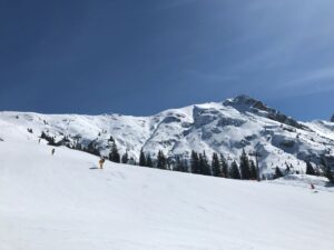 Schneebedeckte Berge unter blauem Himmel, Skifahrer am Hang.