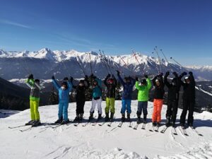 Gruppe von Kindern in Skibekleidung auf einem Berg mit Skiern, sie jubeln.