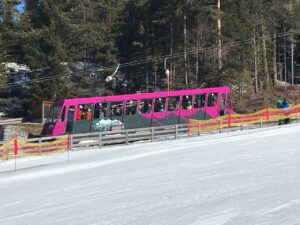 Bunte Gondelbahn mit Fahrgästen im Schnee, umgeben von Wald.