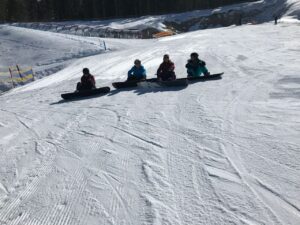 Vier Personen sitzen auf Schlitten auf einer verschneiten Piste.